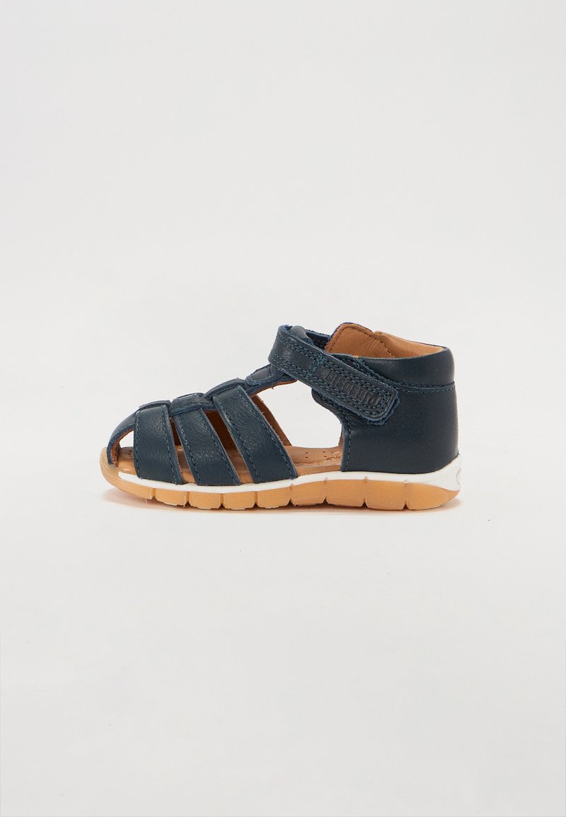 Dark blue leather sandal with open sides, crisscross straps, adjustable Velcro closure, and a light brown rubber sole.