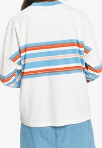 Vit oversized t-shirt med blå, orange och beige horisontella ränder över ryggen. Har rund halsringning och korta ärmar.