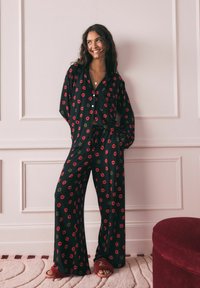 Must mustrekkide komplekt koosneb lõdvalt istuvast, punase ja rohelise huuletrükiga, nööpidega särk koos krae ja laia säärega pükstest.