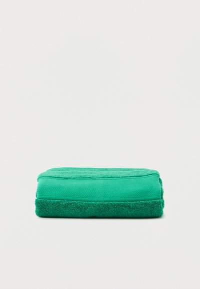 Διπλωμένη πετσέτα λαμπερού πράσινου χρώματος, που ακουμπά επίπεδη σε λευκή επιφάνεια, δείχνοντας απαλή υφή και τακτοποιημένες άκρες.