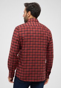 Camicia di flanella a quadri rossi e neri con maniche lunghe, polsini con bottoni e colletto a punta, caratterizzata da una texture liscia e una vestibilità classica.