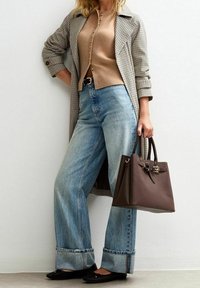 Dlouhý kabát se vzorem kostky, hnědý pletený kardigan, široké světle modré džíny s ohrnutými lemy, černé pohodlné boty a hnědá kabelka.