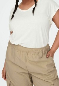 Maglietta bianca a maniche corte abbinata a pantaloni cargo beige chiaro con vita elastica, dotati di tasche laterali e una vestibilità rilassata.