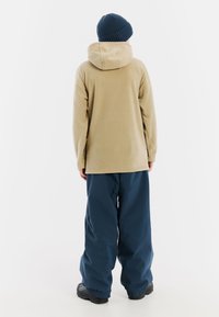 Beige fleecetrui met een capuchon, gecombineerd met losse navyblauwe waterdichte broek en zwarte schoenen. Minimalistisch ontwerp, geen zichtbare patronen.