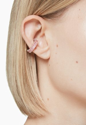 Close-up of a woman's ear featuring a pink gemstone ear cuff, with straight blonde hair framing her face. Smooth skin texture is visible.