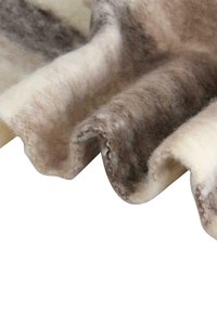 Tissu en laine doux avec un bord ondulé, présentant un mélange de fibres crème, marron clair et grises, affichant une apparence naturelle et texturée.