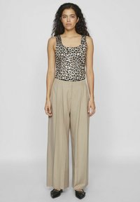 Top senza maniche con stampa leopardata abbinato a pantaloni larghi beige chiaro. Scarpe basse nere completano l'outfit.