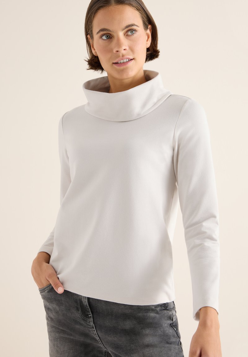 Wit, lange mouw top met een hoge, gevouwen kraag. Zachte stof met een gladde textuur, gecombineerd met grijze spijkerbroek. Eenvoudig en modern ontwerp.