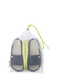 Zapatillas de color azul marino con plantillas beige en una bolsa de malla blanca. Cierre de cuerda en verde brillante con un tope rosa. Forma redondeada con acentos amarillos.