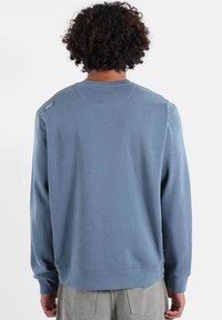 Sweat-shirt bleu clair à col rond et manches longues. Comprend des poignets et un ourlet côtelés, avec un petit logo sur l'épaule arrière.