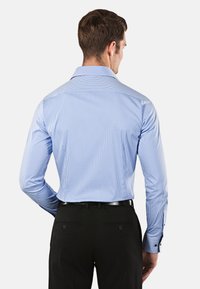 Camicia a maniche lunghe a quadri blu e bianchi con colletto aperto, polsini con bottoni e tessuto liscio, indossata con pantaloni neri.