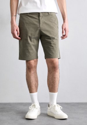 Olivengrønne shorts lavet af bomuld, tætsiddende design, flad front, sidelommer, afsluttet ved knæet, paired med hvide sneakers og sokker.