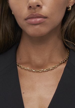 Gouden ketting met ovale schakels en een gepolijste afwerking, gedragen op een donker kledingstuk, wat de glanzende metaaltextuur benadrukt.