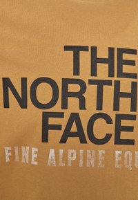 Senfgelbes T-Shirt mit großen schwarzen Buchstaben "THE NORTH FACE" und kleinerem silbernen Text "FINE ALPINE EQP." Glatte Stoffstruktur.