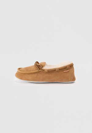 Brown suede moccasin slipper with faux fur lining, a rounded toe, and decorative bow detail. Features a rubber sole and contrasting trim.