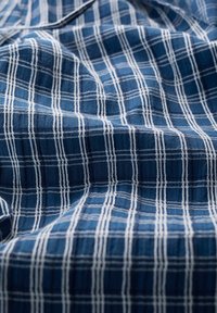 Tissu en coton avec une base bleue et un motif à carreaux blancs, présentant une texture douce et un léger éclat dans le tissu tissé.