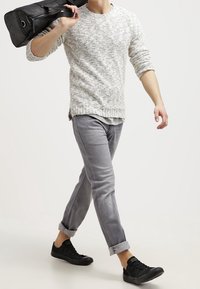 Suéter de punto gris claro con un tejido texturizado, combinado con jeans gris claro arremangados y zapatillas negras. La persona lleva una bolsa negra.