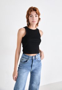 Crna rebrasta crop majica s okruglim izrezom, u kombinaciji s svijetloplavim trapericama visokog struka širokih nogavica koje imaju prednje džepove.