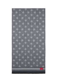 Couverture grise à motifs comportant des courbes entrelacées, texture douce, et une étiquette rouge en bas. Bords finement finis avec un tissu foncé.