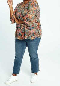 Haut à imprimé cachemire multicolore avec manches trois-quarts, associé à un jean en denim bleu et des baskets blanches. Coupe décontractée.