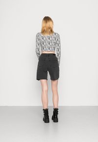 Calções de ganga pretos com bainha desfiada, combinados com uma blusa de mangas compridas branca com um padrão de riscas de zebra pretas. Botas pretas até ao tornozelo.