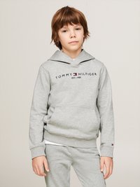 Felpa grigia con cappuccio, coulisse e tasca frontale, con la scritta "TOMMY HILFIGER EST. 1985" in blu scuro. Indossata con pantaloni grigi abbinati.