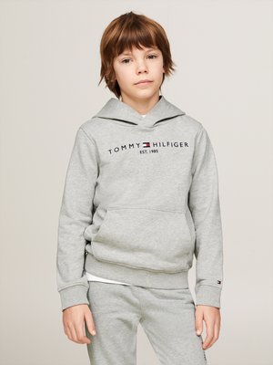 Sudadera gris con cordón y bolsillo frontal, que presenta "TOMMY HILFIGER EST. 1985" en azul oscuro. Se lleva con pantalones grises a juego.
