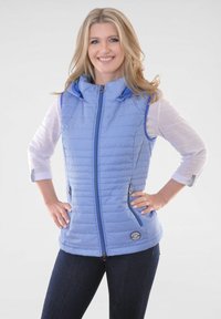 Blaues gepolstertes Weste mit Kapuze, mit einem Diamantenmuster, kontrastierendem Reißverschluss und Reißverschlusstaschen. Getragen über einem weißen Langarmshirt.
