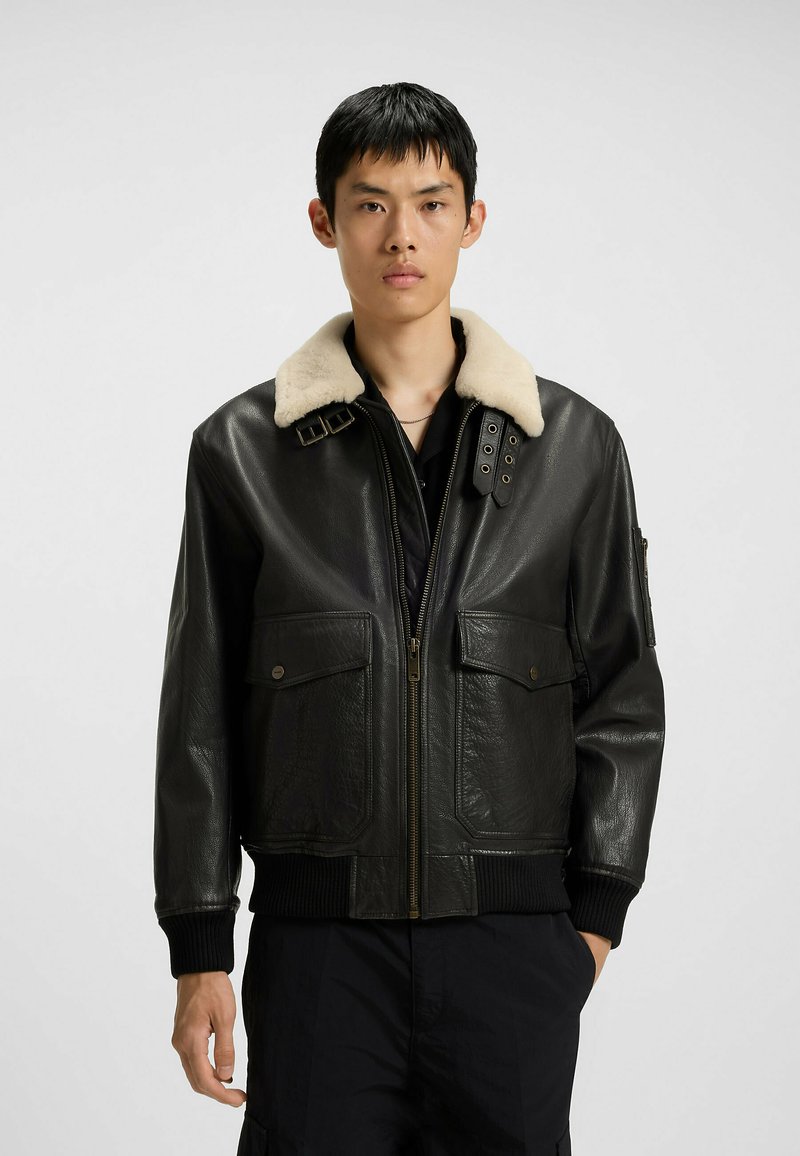 Czarna skórzana kurtka bombowiec z beżowym kołnierzem z sztucznego futra, z przodu na zamek błyskawiczny i dwoma kieszeniami na piersi. Żebrowane mankiety i dolna krawędź dopełniają całość.