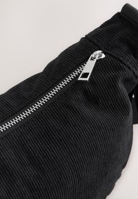 Zwarte ribfluwelen tas met een rits met metalen beslag, gestructureerde stof en een afgeronde vorm, met de verticale geribbelde patroon duidelijk zichtbaar.