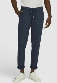 Marineblaue, dehnbare Jogginghosen aus Baumwolle mit elastischem Bund, Kordelzug, Seitentaschen und umgeschlagenen Beinabschlüssen; getragen mit weißen Sneakers.