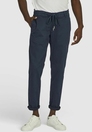 Marineblaue, dehnbare Jogginghosen aus Baumwolle mit elastischem Bund, Kordelzug, Seitentaschen und umgeschlagenen Beinabschlüssen; getragen mit weißen Sneakers.