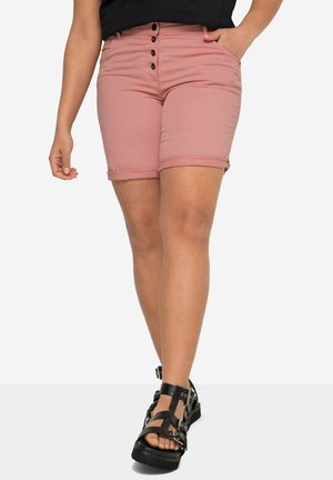 Shorts en denim rose clair, devant boutonné, avec un ourlet roulé et des poches. Portés avec des sandales noires à lanières avec des accents métalliques.