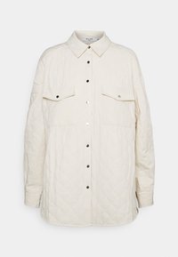 Chaqueta de camisa acolchada color crema con cuello, dos bolsillos en el pecho y botones a presión plateados. Textura suave con un patrón de diamantes en toda la prenda.