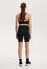 Fekete sportmelltartó, keresztezett pántokkal, fekete, testhezálló sorttal párosítva. A modellen fekete sportcipő és rövid zokni van.