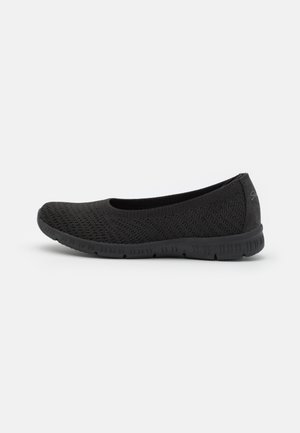 Sort strikket stof slip-on flad sko med tekstureret sål og afrundet tå, set fra siden på hvid baggrund.