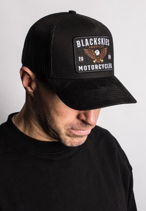 Schwarze Kappe mit Netzrücken, versehen mit einem auffälligen Aufnäher mit dem Schriftzug "BLACKSKIES AMERICAN MOTORCYCLES" und einem Adlerdesign in Braun- und Goldtönen.