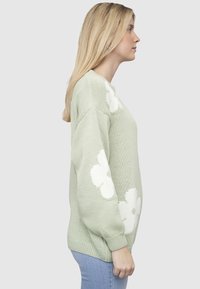 Heleheline kootud kampsun valgete lillemustritega varrukatel, soonikkoes mansettide ja lõdva lõikega. Tekstureeritud materjal ja vabaaja stiil.