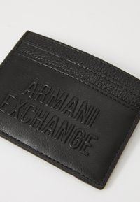 Juodas odinis kortelių dėklas su reljefiniu „ARMANI EXCHANGE“ logotipu, tekstūriniais akcentais ir kortelių vietomis viršuje.