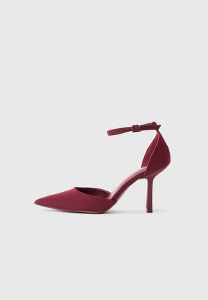 Escarpin bordeaux à bout pointu avec bride de cheville et talon aiguille étroit sur fond blanc uni.