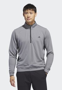 Pull-over gris à manches longues et demi-zip, fabriqué en tissu texturé. Présente une fermeture éclair noire et un logo Adidas sur la poitrine gauche.