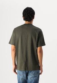 Tricou scurt cu mânecă scurtă, de culoare verde închis, într-o croial�ă lejeră, cu guler rotund. Material din bumbac neted cu un detaliu de cusătură discret pe spate.