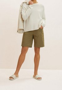 Lichtbeige geribde trui, olijfgroene korte broek en grijze gewatteerde instapsandalen. Casual outfit met een relaxte pasvorm en zachte texturen.