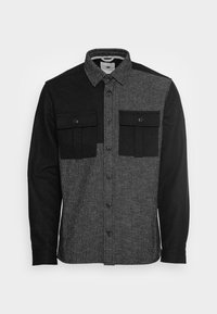 Sort og grå flannel skjorte med et ternet mønster på den ene side, ensfarvet sort på den anden, to forsøgte lommer og knaplukning.