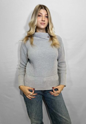 Maglione lavorato a maglia grigio chiaro con collo a scialle, caratterizzato da un orlo e polsini a coste. Indossato con jeans blu, mostrando una vestibilità rilassata.