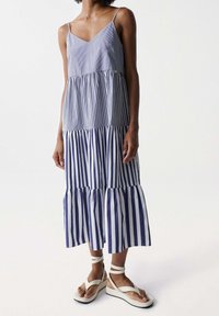 Pruhované bezramínkové šaty s rozšířenou spodní částí, s modro-bílými svislými pruhy. Nosené s bílými platformovými sandály.