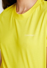 Žluté bavlněné tričko s kulatým výstřihem, na prsou s malým bílým logem "Calvin Klein". Měkká textura a volný střih.