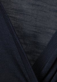 Detailní záběr tmavě modré pletené tkaniny s překrývajícími se vzory ve tvaru V a viditelnými stehenními texturami.