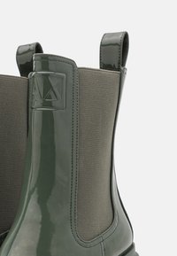 Botas Chelsea verdes brillantes con paneles laterales elásticos, que presentan un tejido texturizado y un acento de logo en el talón para mayor agarre y estilo.