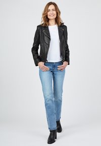 Svart läderjacka med en figursydd design, över en vit t-shirt, kombinerat med ljusblå raka jeans och svarta klackade ankelstövlar.